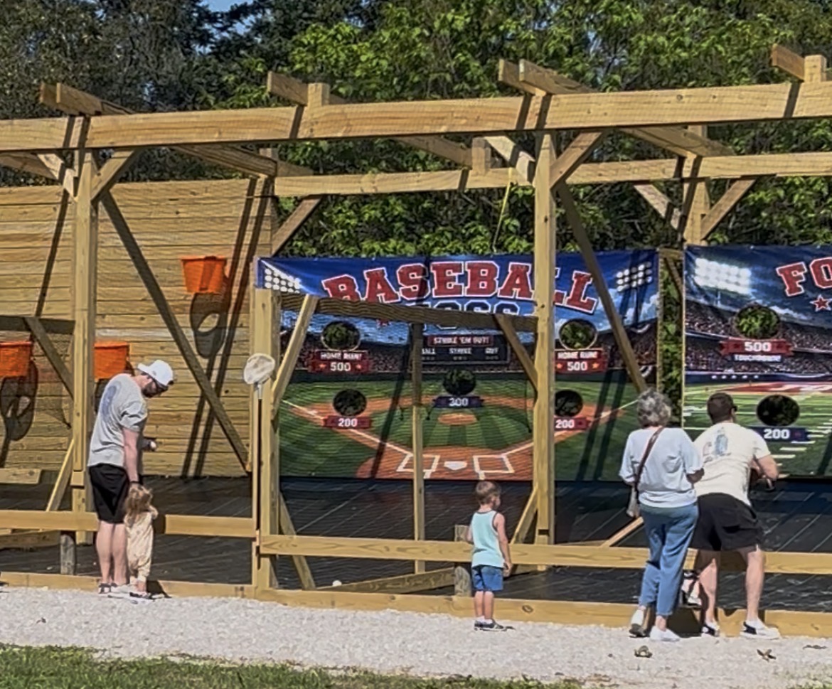 Families tossing balls at the baseball and football target boards